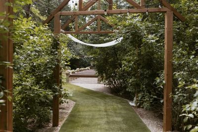 Wooden garden archway leads to outdoor wedding venue, surrounded by lush greenery and a green grass aisle.