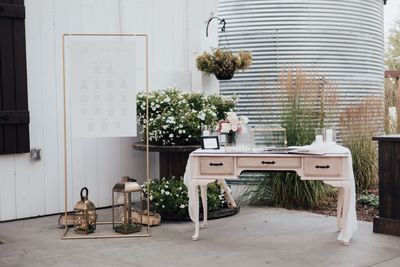 Rustic wedding decor with seating chart, lanterns, flowers, and guestbook on vintage table beside greenery backdrop.