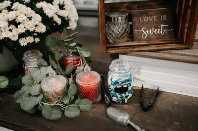 Assorted candies in glass jars with flowers and Love is sweet sign at rustic wedding candy table.