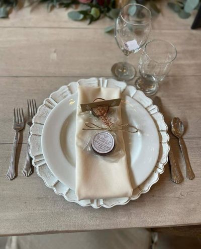 Elegant table setting with white plate, cream napkin, and glassware on rustic wooden table. Perfect for weddings or events.