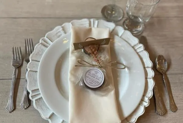 Elegant table setting with white plate, cream napkin, and glassware on rustic wooden table. Perfect for weddings or events.